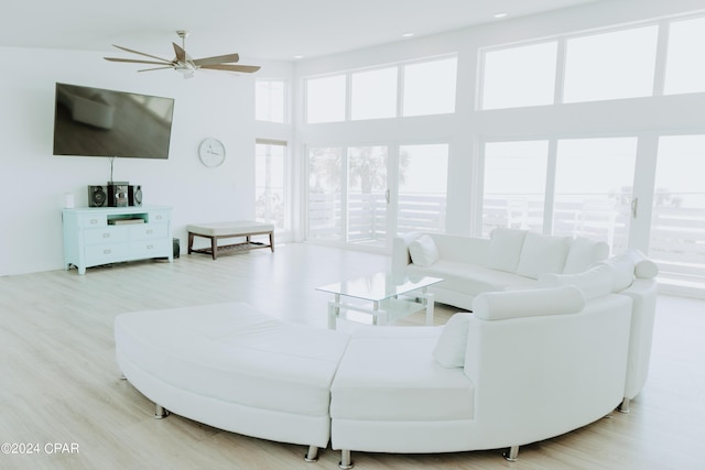 living room with a towering ceiling, light wood-style flooring, and a ceiling fan