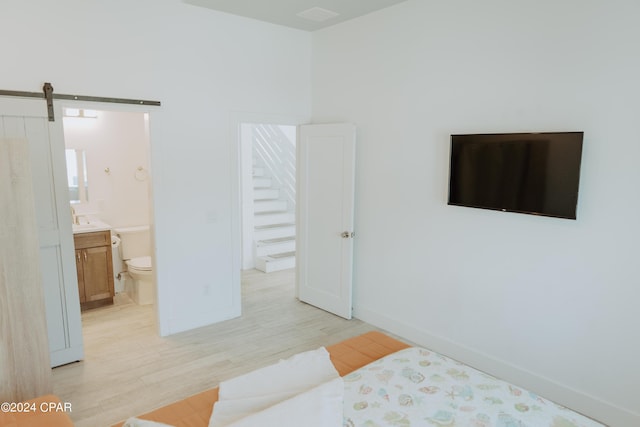 bedroom with ensuite bathroom, a barn door, light wood-style flooring, and baseboards