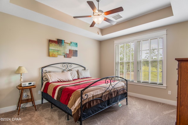 bedroom featuring a raised ceiling, light colored carpet, and ceiling fan