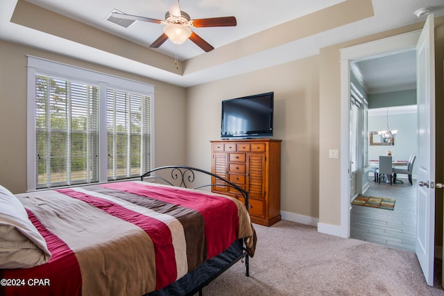 bedroom with light colored carpet, ceiling fan with notable chandelier, and a tray ceiling