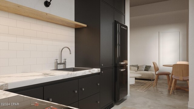 kitchen with light stone countertops, tasteful backsplash, black fridge, and sink