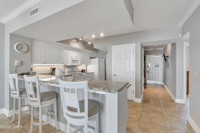 kitchen with white appliances, visible vents, a peninsula, white cabinets, and crown molding