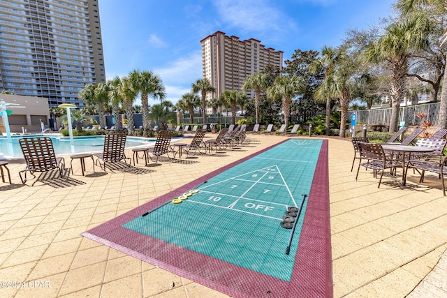 view of property's community featuring a swimming pool, a patio, shuffleboard, and fence