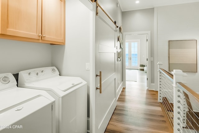 clothes washing area featuring a barn door, washing machine and dryer, cabinets, and light hardwood / wood-style floors