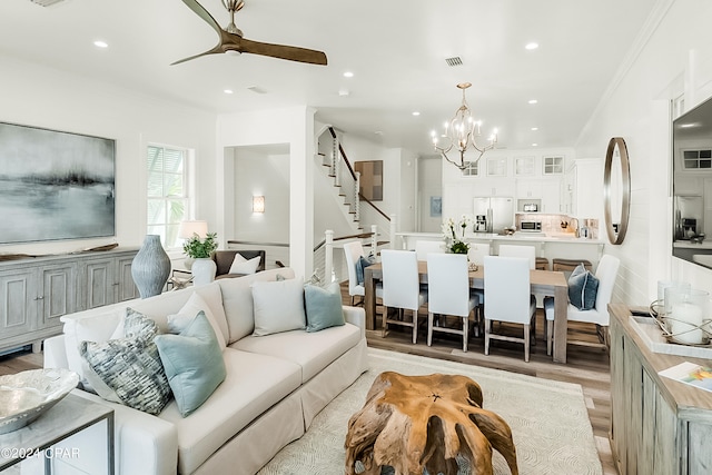 living room with ornamental molding, ceiling fan with notable chandelier, and light wood-type flooring