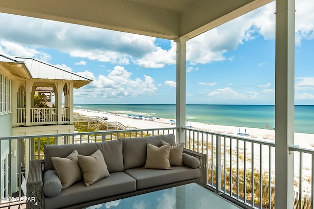 balcony with an outdoor hangout area, a water view, and a view of the beach