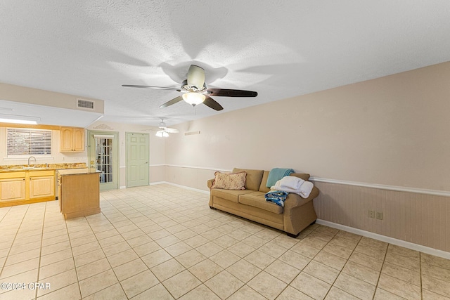 unfurnished living room featuring light tile floors, a textured ceiling, ceiling fan, and sink