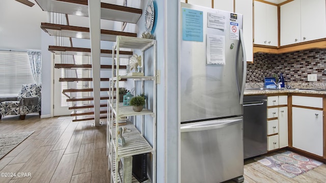 kitchen featuring decorative backsplash, appliances with stainless steel finishes, wood tiled floor, white cabinetry, and a sink