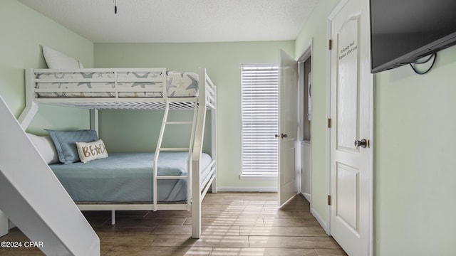 bedroom featuring baseboards, a textured ceiling, and wood finish floors