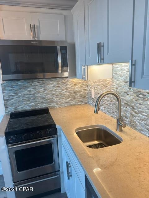 kitchen with white cabinets, sink, tasteful backsplash, light stone counters, and stainless steel appliances