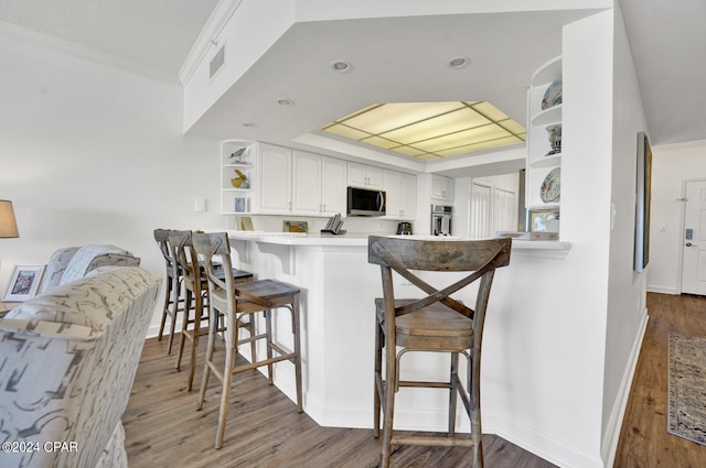 kitchen with kitchen peninsula, appliances with stainless steel finishes, dark wood-type flooring, white cabinets, and a breakfast bar