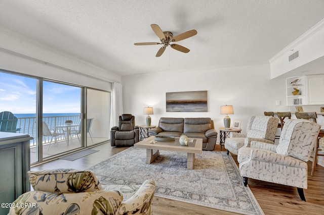 living room featuring light hardwood / wood-style flooring, a water view, ornamental molding, ceiling fan, and a textured ceiling