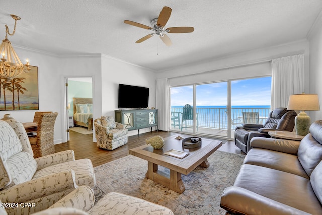 living room with a water view, a textured ceiling, ceiling fan with notable chandelier, dark wood-type flooring, and crown molding