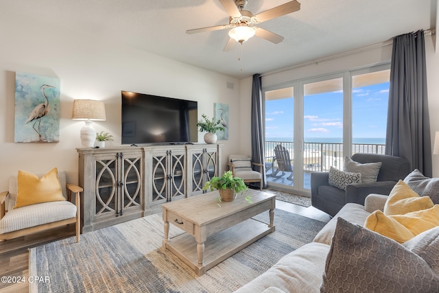 living room with a water view, ceiling fan, hardwood / wood-style flooring, and a textured ceiling