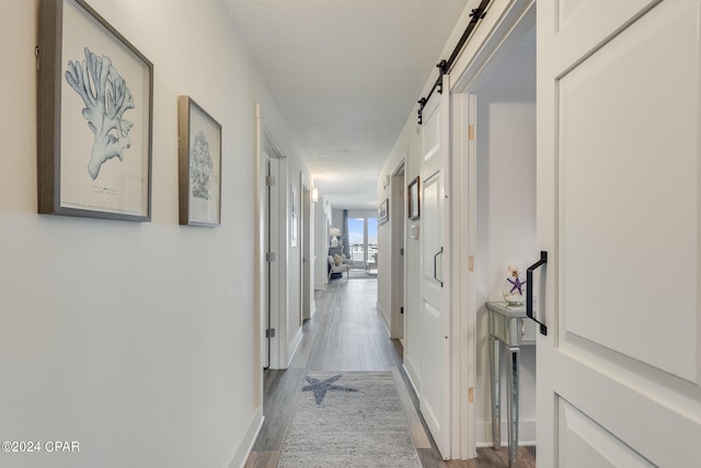 corridor featuring a textured ceiling, a barn door, and light wood-type flooring