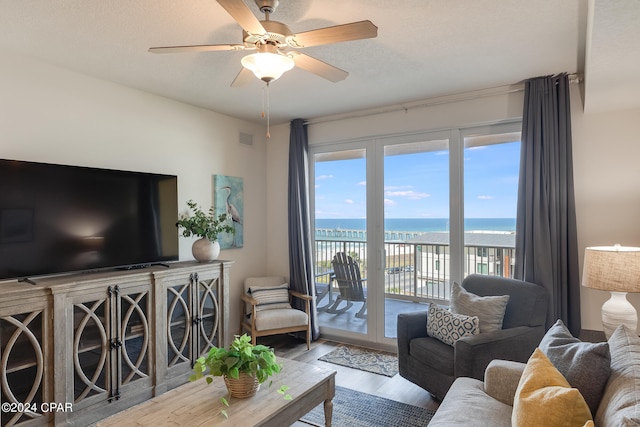 living room featuring a textured ceiling, a water view, hardwood / wood-style floors, and ceiling fan