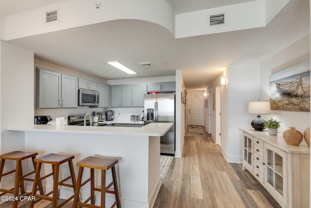 kitchen featuring appliances with stainless steel finishes, a breakfast bar, kitchen peninsula, and light hardwood / wood-style floors