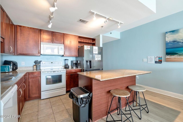 kitchen featuring white appliances, light stone countertops, light tile patterned floors, a kitchen island, and a kitchen bar