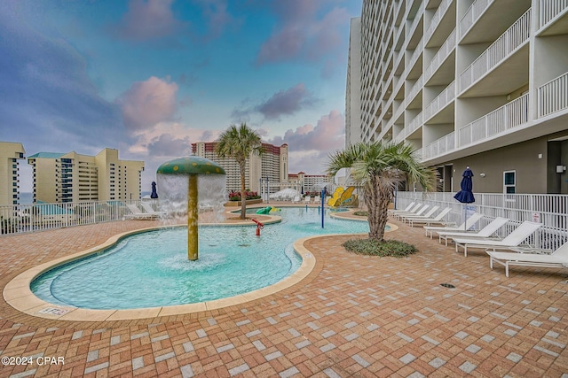 pool at dusk featuring pool water feature and a patio