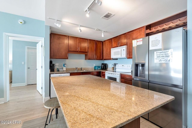 kitchen featuring sink, light stone counters, a center island, a kitchen breakfast bar, and white appliances