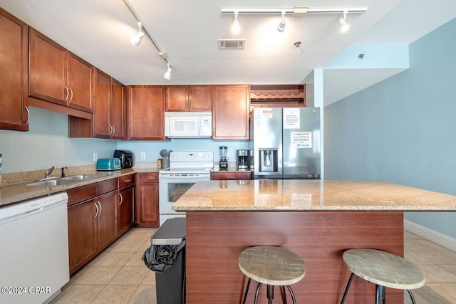 kitchen with light tile patterned flooring, white appliances, a breakfast bar, and sink