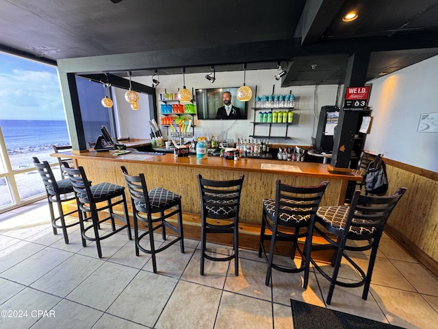 bar featuring hanging light fixtures, a water view, expansive windows, and light tile floors