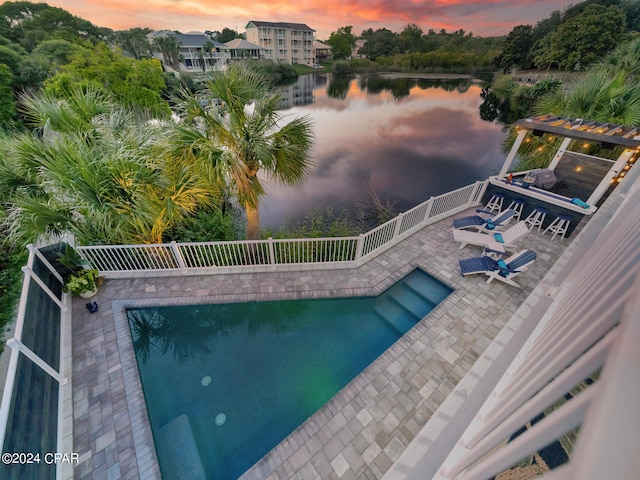 pool at dusk featuring a patio area and a water view