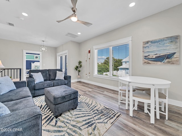 living room featuring ceiling fan with notable chandelier and light hardwood / wood-style floors