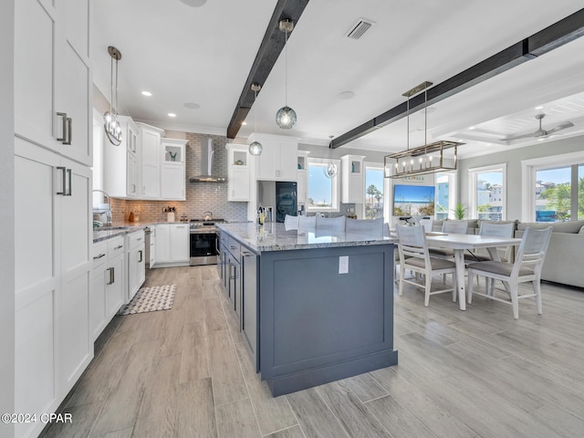 kitchen featuring stainless steel range, wall chimney range hood, beamed ceiling, white cabinetry, and hanging light fixtures