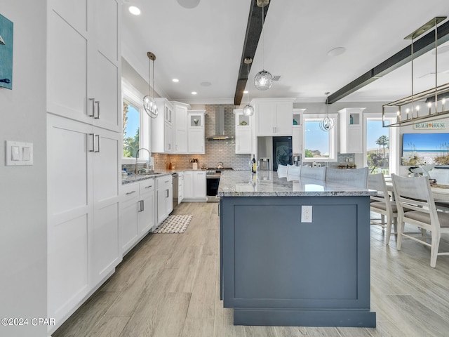 kitchen featuring beam ceiling, stainless steel appliances, wall chimney range hood, white cabinets, and light wood-type flooring