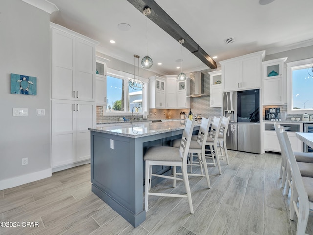 kitchen featuring stainless steel fridge, wall chimney range hood, a center island, light hardwood / wood-style floors, and white cabinetry