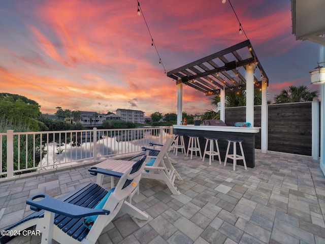 patio terrace at dusk featuring a pergola, a water view, and an outdoor bar