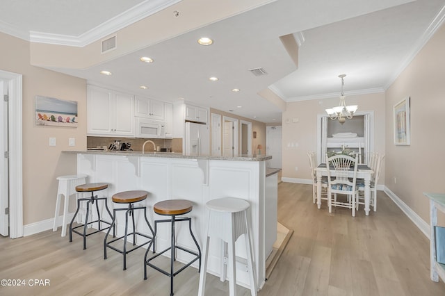 kitchen with kitchen peninsula, white appliances, hanging light fixtures, light stone countertops, and white cabinets