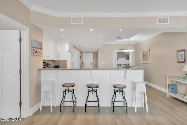 kitchen featuring a kitchen bar, light stone countertops, white cabinetry, and kitchen peninsula