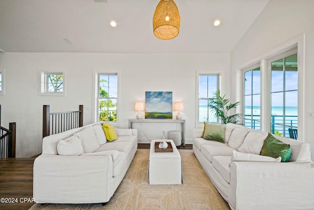 living room with plenty of natural light, light hardwood / wood-style floors, a water view, and vaulted ceiling