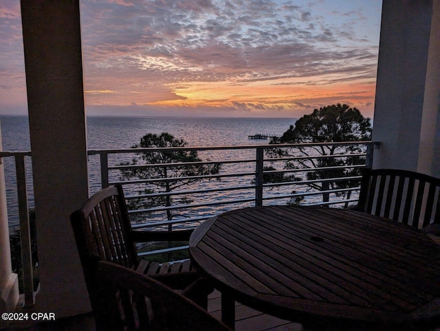 balcony at dusk featuring a water view