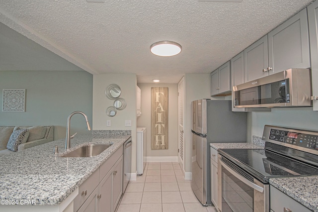 kitchen featuring light tile floors, gray cabinets, light stone counters, and stainless steel appliances