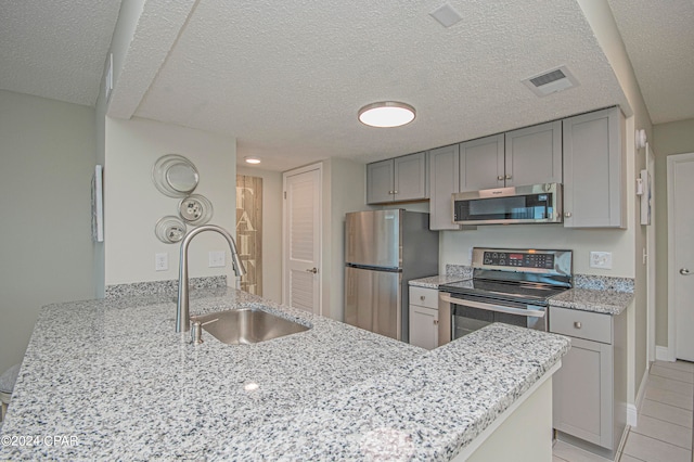 kitchen featuring appliances with stainless steel finishes, light stone counters, light tile floors, a textured ceiling, and sink