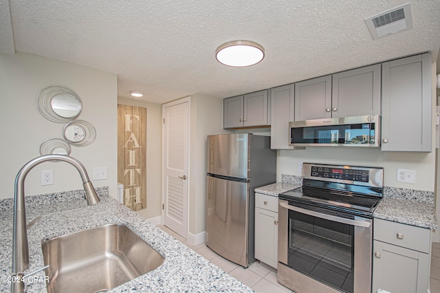 kitchen featuring light stone countertops, sink, stainless steel appliances, light tile floors, and a textured ceiling