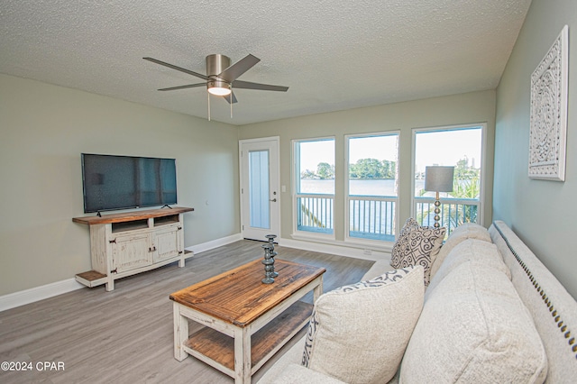 living room with a textured ceiling, ceiling fan, and light wood-type flooring