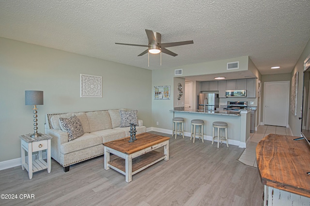 living room featuring a textured ceiling, light hardwood / wood-style floors, and ceiling fan