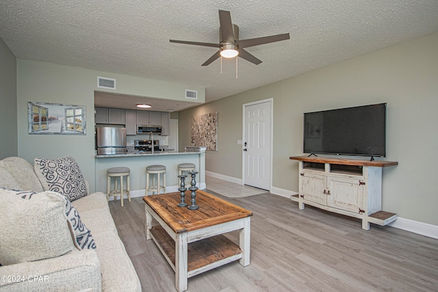 living room featuring ceiling fan, light wood-type flooring, and a textured ceiling