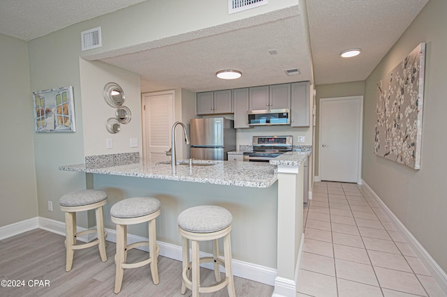 kitchen featuring stainless steel appliances, gray cabinetry, a kitchen breakfast bar, sink, and kitchen peninsula