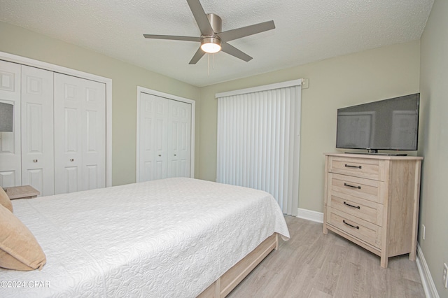 bedroom featuring ceiling fan, two closets, a textured ceiling, and light hardwood / wood-style floors