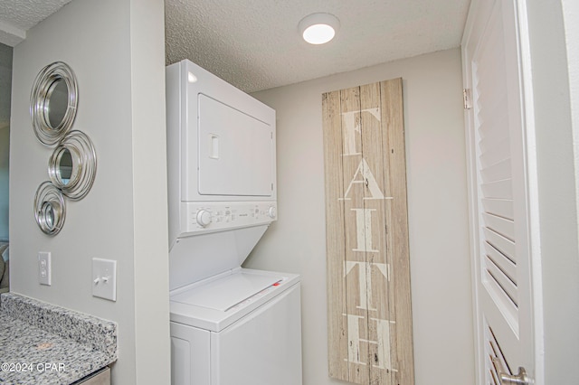 laundry area with a textured ceiling and stacked washer / drying machine