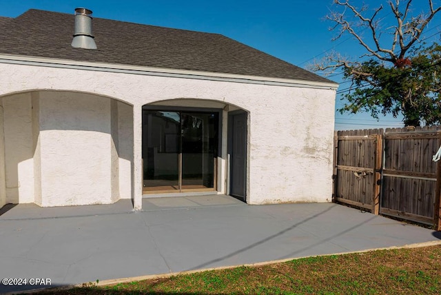 rear view of property with roof with shingles, a patio, stucco siding, a gate, and fence