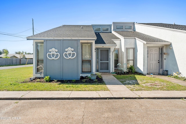 view of front of home with a front yard, roof with shingles, fence, and stucco siding