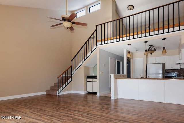 unfurnished living room with stairway, wood finished floors, a towering ceiling, and baseboards