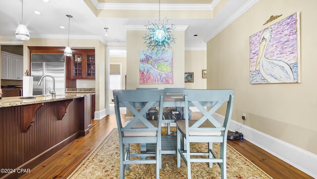 dining area with hardwood / wood-style floors, ornamental molding, sink, and a tray ceiling