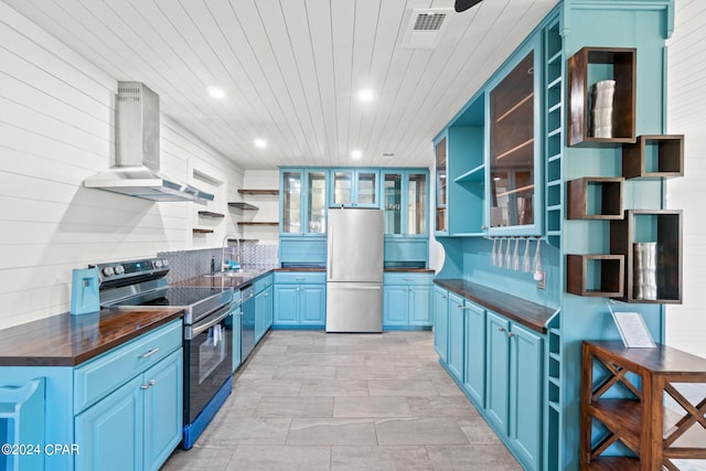 kitchen featuring blue cabinetry, appliances with stainless steel finishes, wall chimney range hood, wooden ceiling, and sink